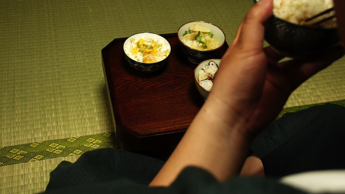 膳から茶漬けの椀を手に取り、箸で食べているところ