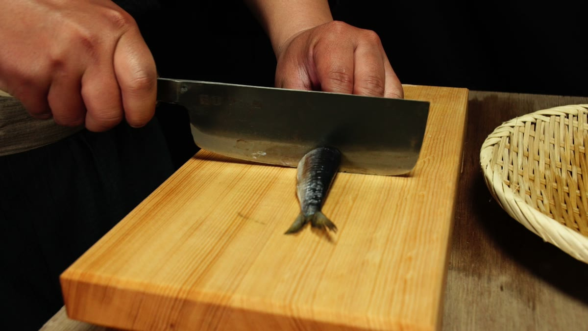 まな板の上のイワシに包丁を入れて切り分けるところ