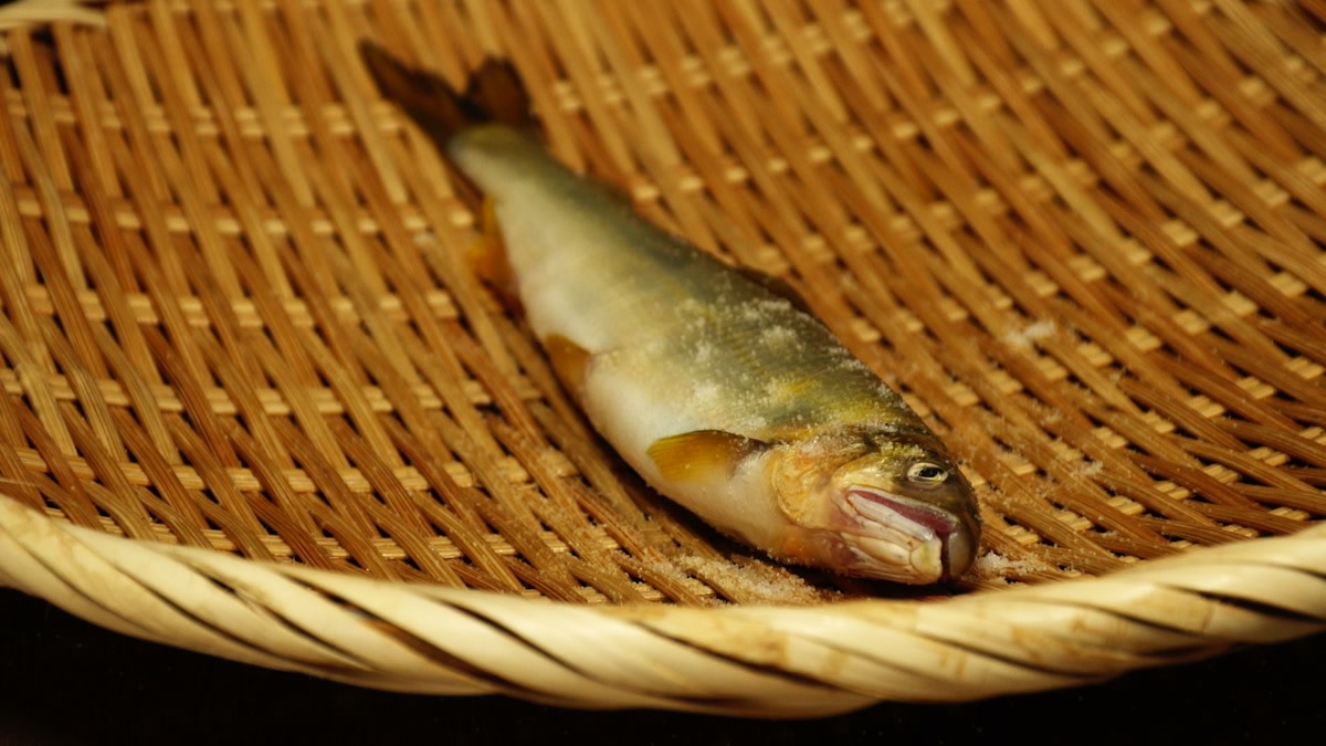 竹ざるの上に置かれた鮎一尾。表面に塩の粒がついている