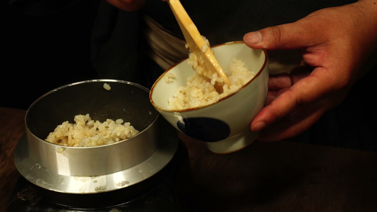 炊きあがった玄米を、羽釜から椀へ木のしゃもじでよそっているところ