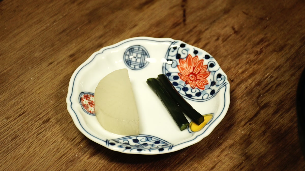 白地に藍と朱の絵付けの小皿に盛られた大根と蕨の煮物
