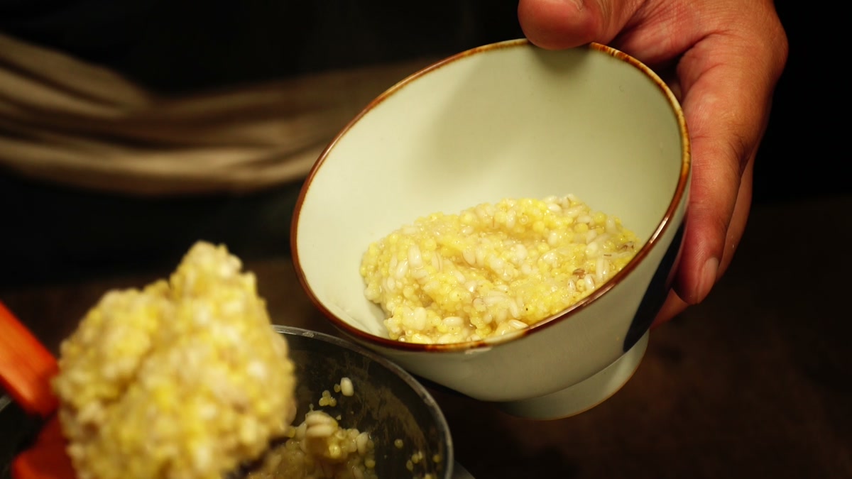 炊きあがった黄色い雑穀粥を椀によそっているところ