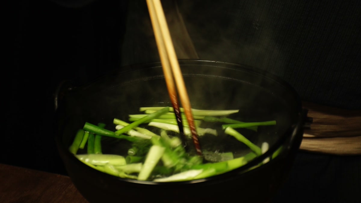 湯気の立つ鍋の中で、切ったネギを菜箸でまぜているところ