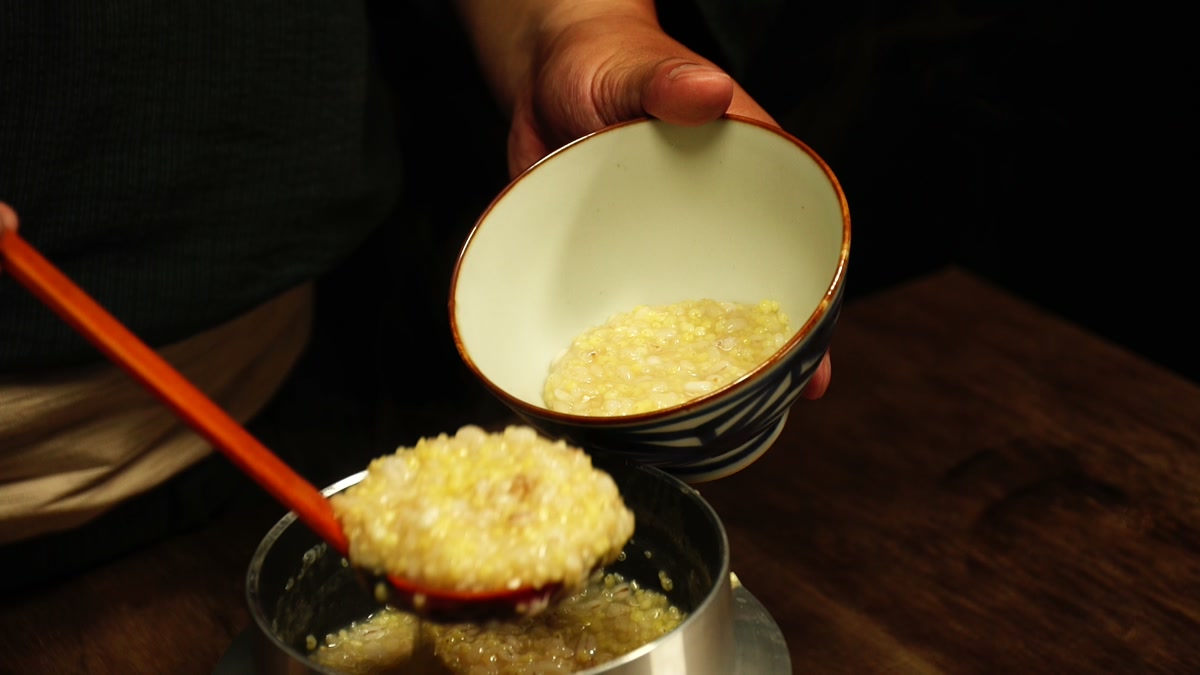 羽釜から玄米と雑穀の粥をすくい、椀へよそっているところ