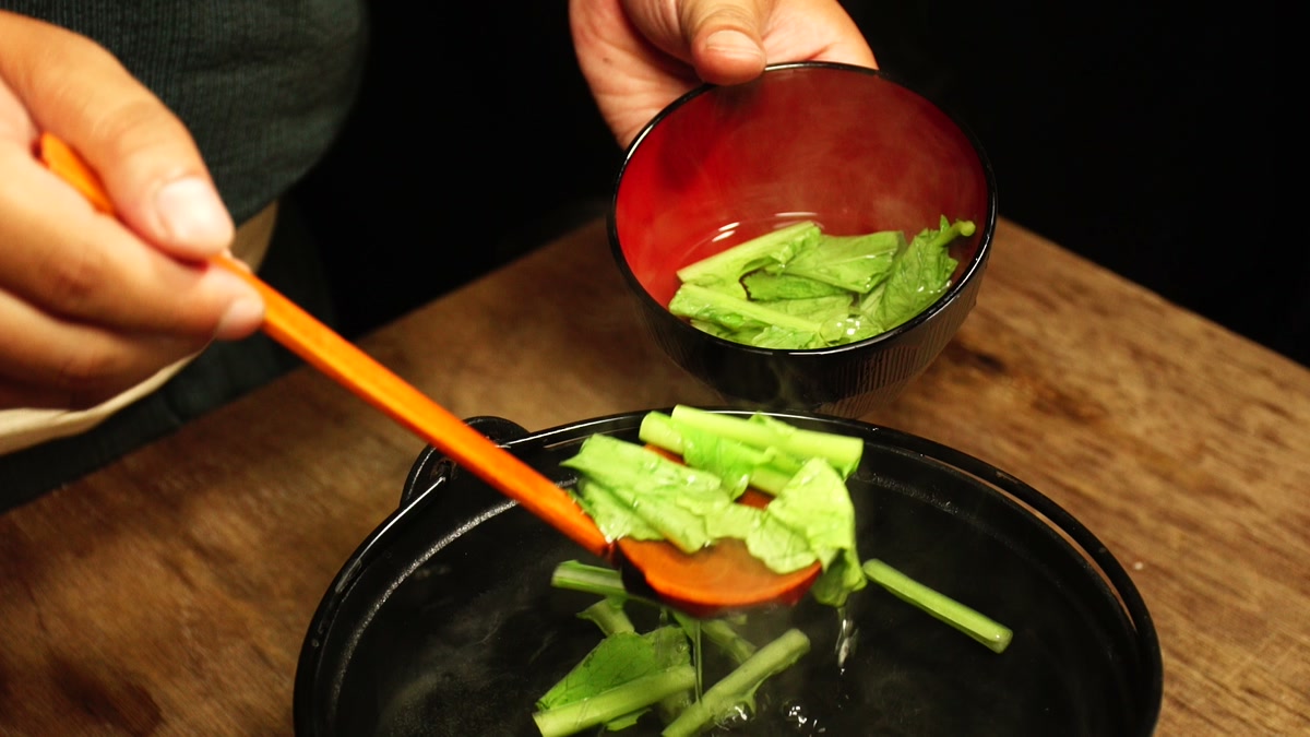 鍋から青菜をすくい、椀へ盛りつけているところ