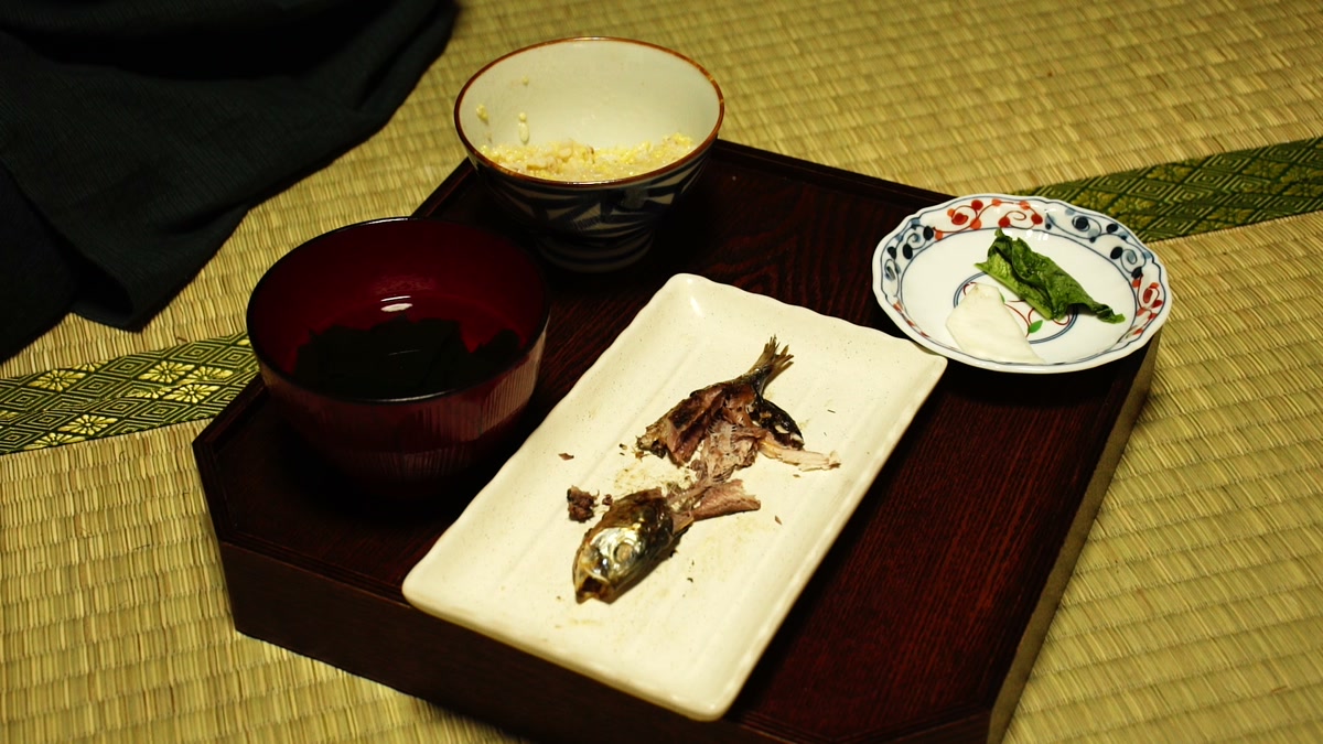 畳に据えた膳。粥の椀、汁椀、食べ終えた鰯の皿、漬物の小皿が並ぶ