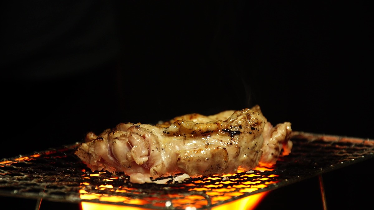 炭火の網の上で鶏もも肉を塩で焼いていく