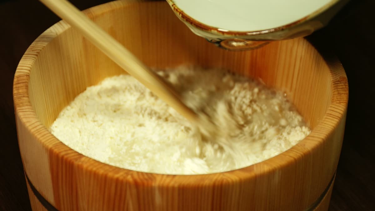 桶に入れたうどん粉に水を少しずつ加えて混ぜる