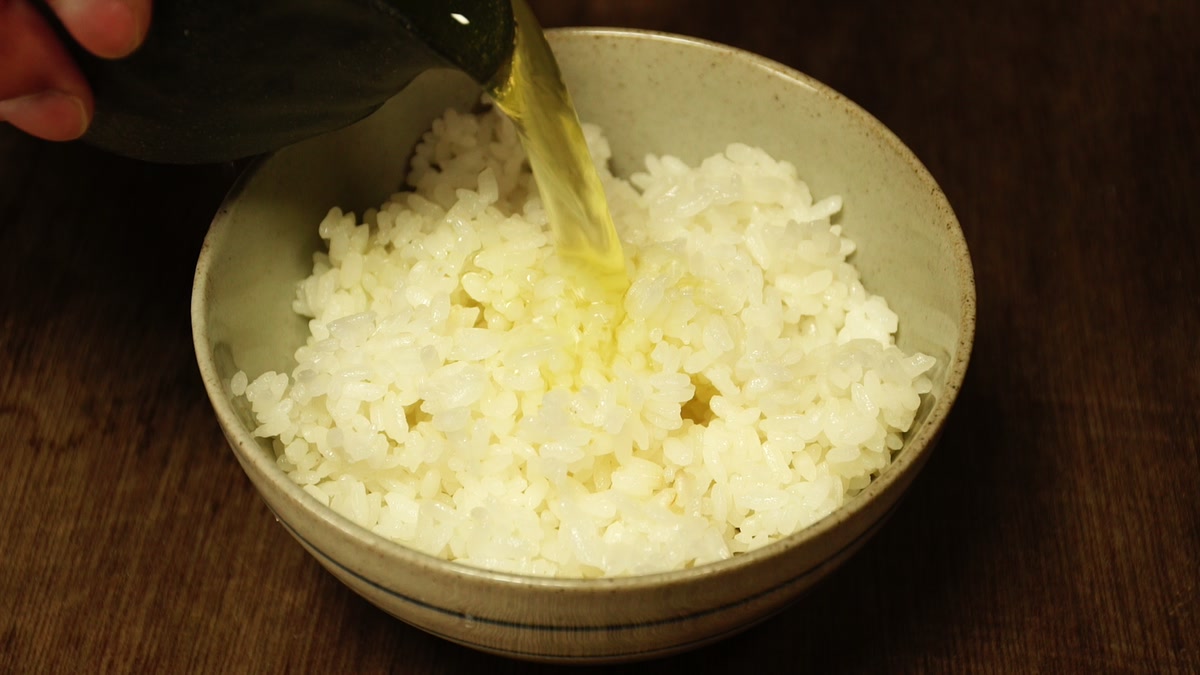 椀によそった飯に、注ぎ口のある器から煎茶を注いでいるところ