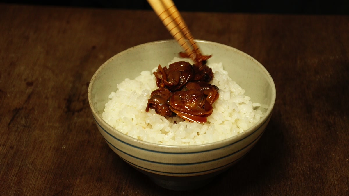 椀によそった冷や飯の上に、箸でハマグリの時雨煮をのせているところ